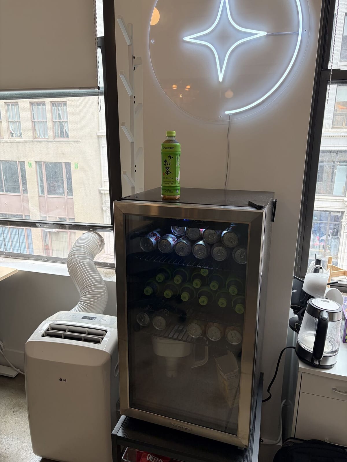 Arcjet neon spark sign above a glass-door mini fridge stocked with green tea and Diet Coke in the New York office